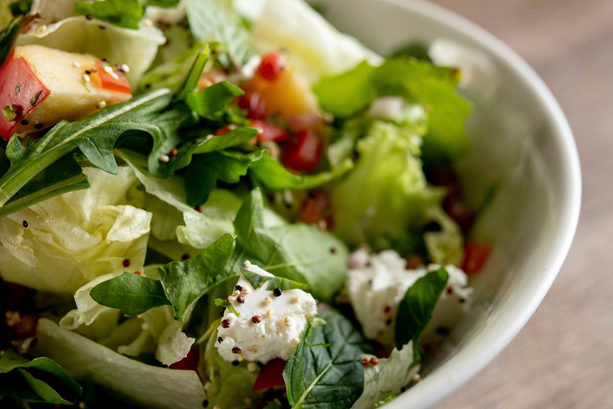 A cup of steaming lemon balm tea on a wooden table surrounded by fresh herbs